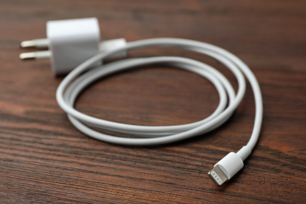 Bloc chargeur USB-C blanc et câble Lightning enroulé posés sur une table en bois